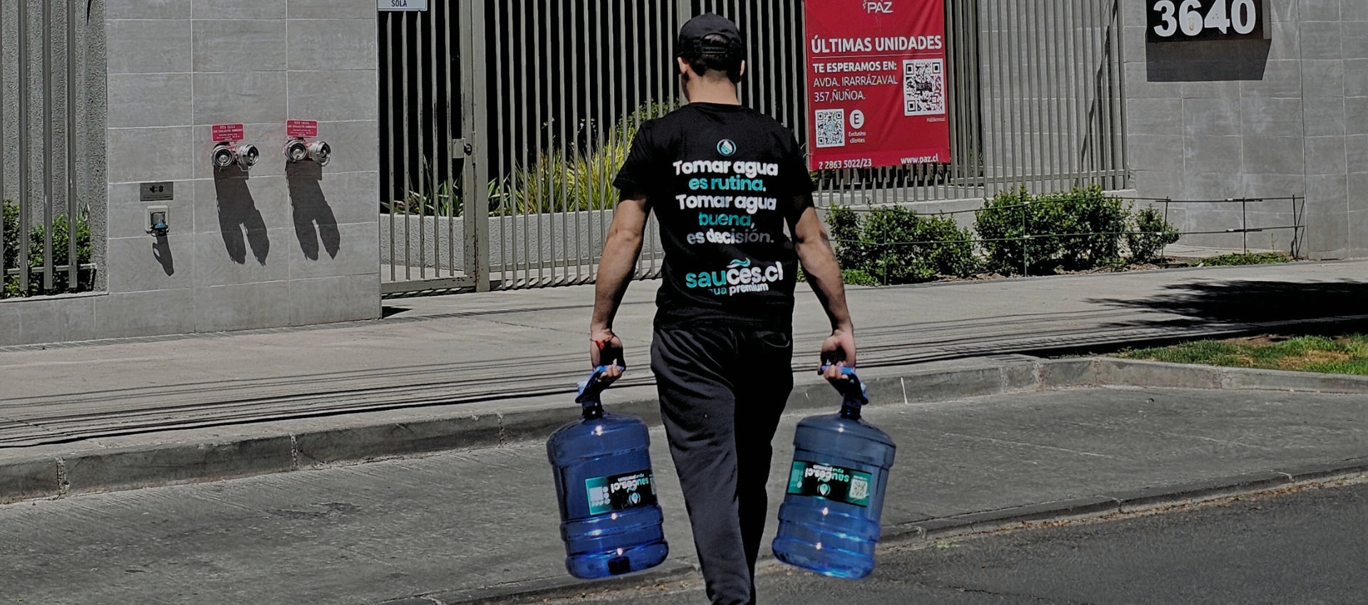 Repartidor de Sauces cruzando la calle para entregar bidones de agua purificada en edificio residencial cerca de Avenida Irarrázaval, Ñuñoa.