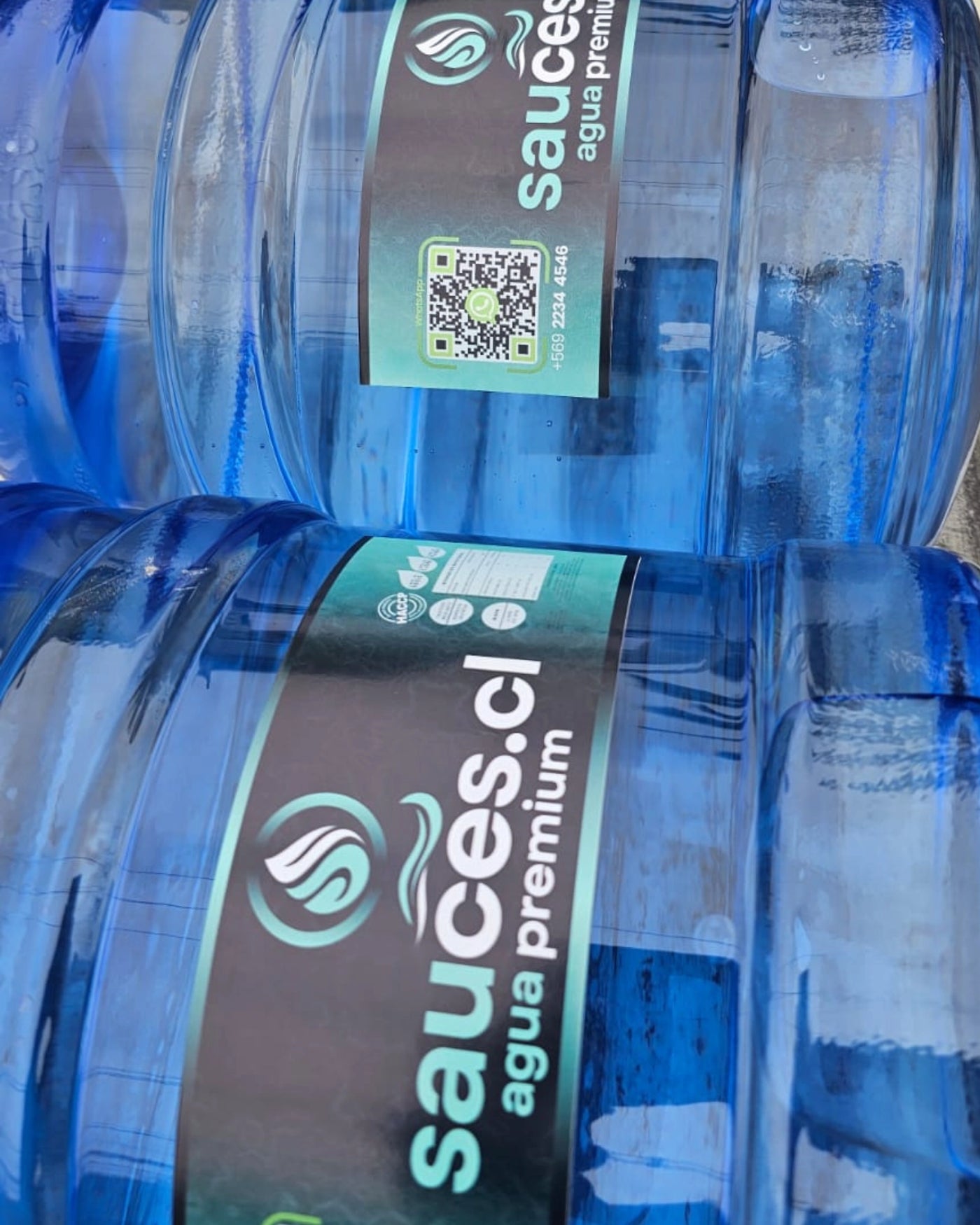 Etiqueta Sauces.cl agua premium en primer plano sobre bidones apilados