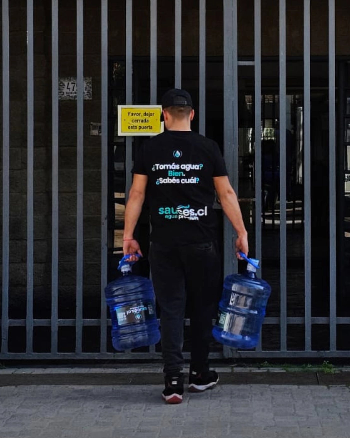 Repartidor Sauces.cl llevando dos bidones de 20 litros hasta la puerta de un domicilio